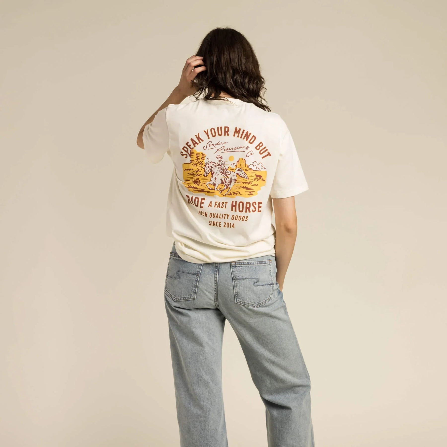 Person wearing a white t-shirt with a graphic and text, standing against a beige background